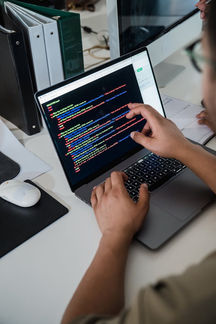 about-us-02 Close-up of a programmer pointing at a colorful code script on a laptop in an office setting.